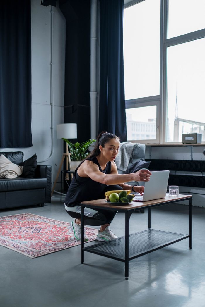 Home Woman using laptop while exercising at home, featuring a modern gym setting.